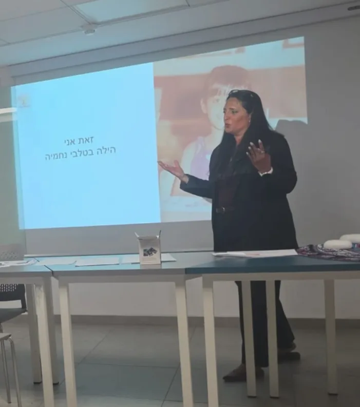 הילה מציגה מול מסך מוקרן באולם מפגשים